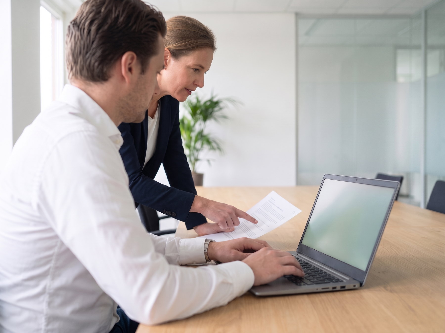 Deelnemer werkt op een laptop aan een praktijkopdracht met een eigen document, terwijl de trainer een werkblad aanwijst.